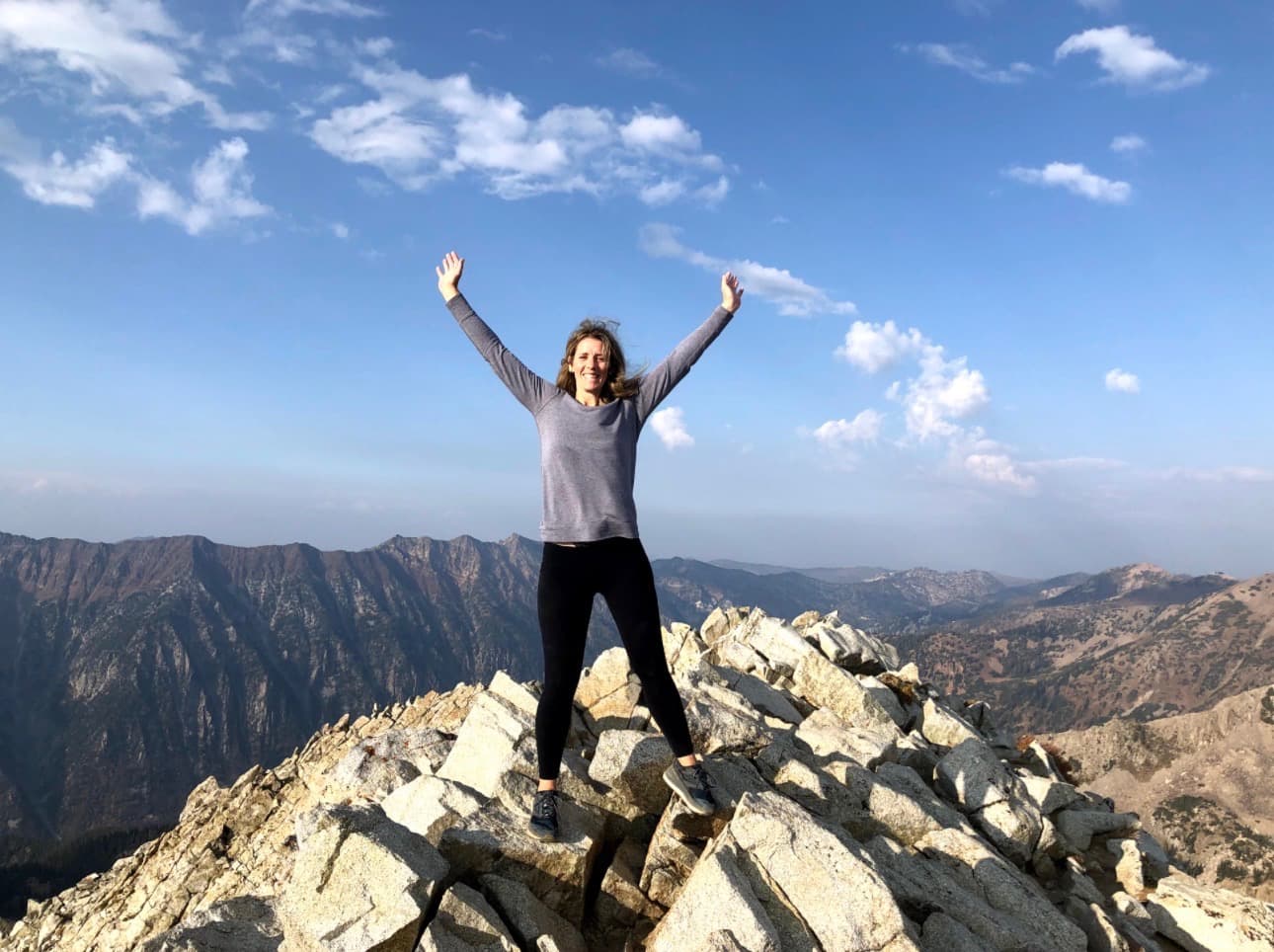 Tomi Kennedy on a Wasatch mountain summit, arms raised in celebration